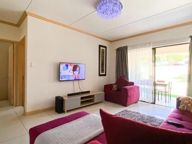 A bright living room featuring tiled flooring and a sliding glass door that provides access to the outdoor patio area.