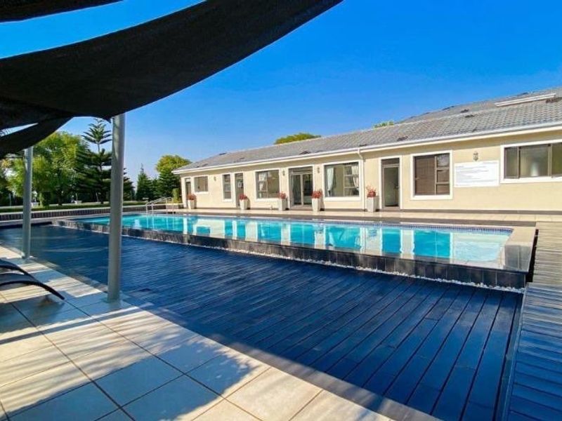 A well-maintained outdoor pool area featuring a large swimming pool, timber decking, and a shade sail structure, perfect for relaxation and entertainment.