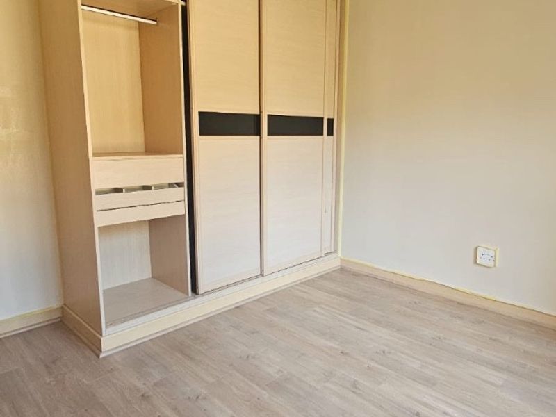 A clean, empty bedroom featuring light-toned laminate flooring and a large, modern built-in wardrobe with sliding doors.