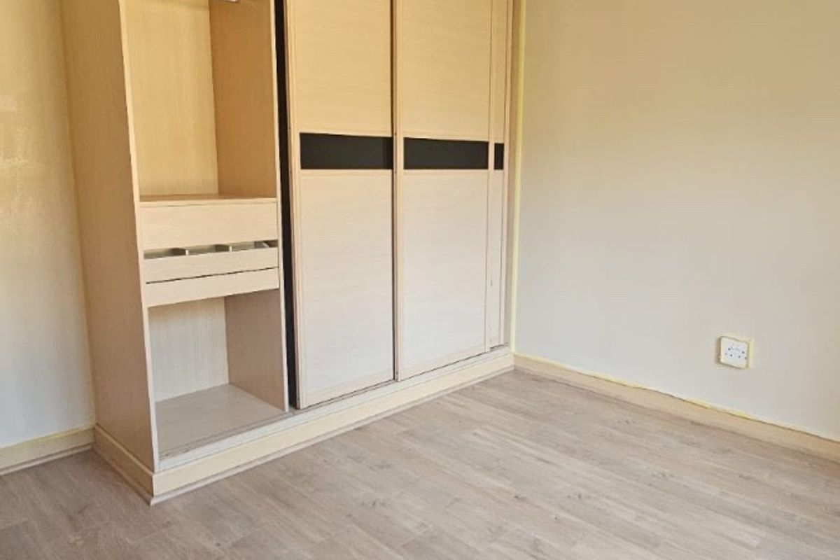 A clean, empty bedroom featuring light-toned laminate flooring and a large, modern built-in wardrobe with sliding doors.