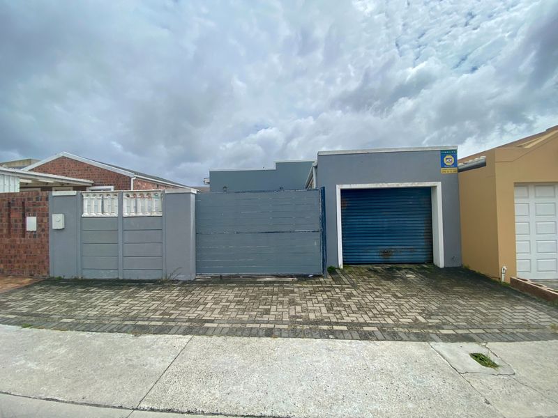 Front exterior view featuring a paved driveway, a single garage with a roller shutter door, and a secure boundary wall with a pedestrian gate.