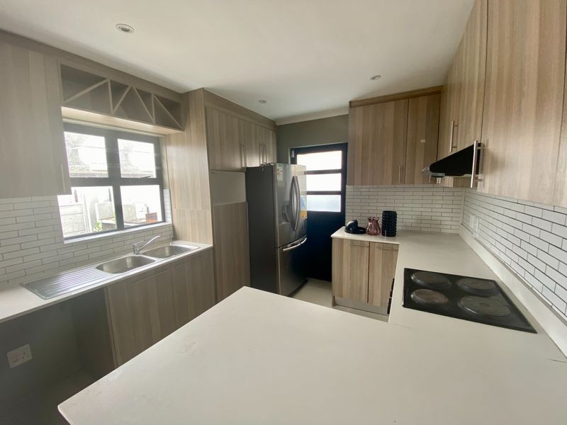 Modern kitchen featuring light wood-grain cabinetry, stone countertops, subway tile backsplash, and integrated electric hob with extractor fan.