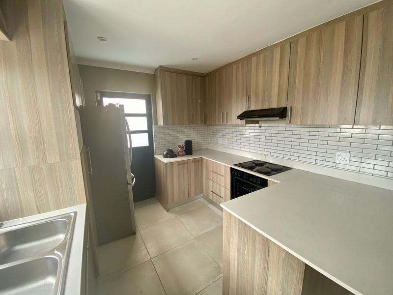 Modern kitchen featuring wood-look cabinetry, stone countertops, subway tile backsplash, and integrated appliances including an electric hob and oven.