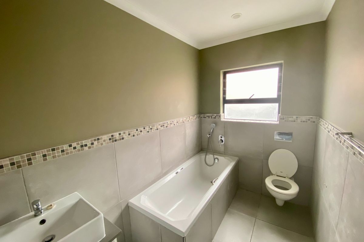 A clean, functional bathroom featuring a built-in bathtub, wall-mounted toilet, and a modern basin with neutral wall and floor tiling.