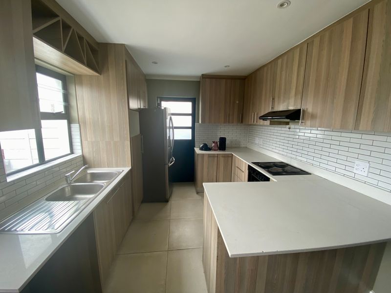 Modern kitchen featuring wood-look cabinetry, stone countertops, subway tile backsplash, and integrated appliances, offering a clean and functional workspace.