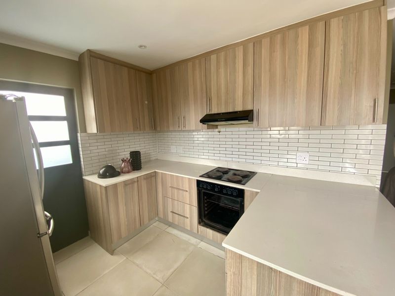 Modern kitchen featuring wood-look cabinetry, stone countertops, subway tile backsplash, and integrated electric cooking appliances.