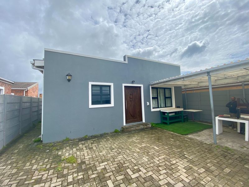 Rear exterior view featuring a paved courtyard, covered patio area with a built-in braai, and secure boundary walling.