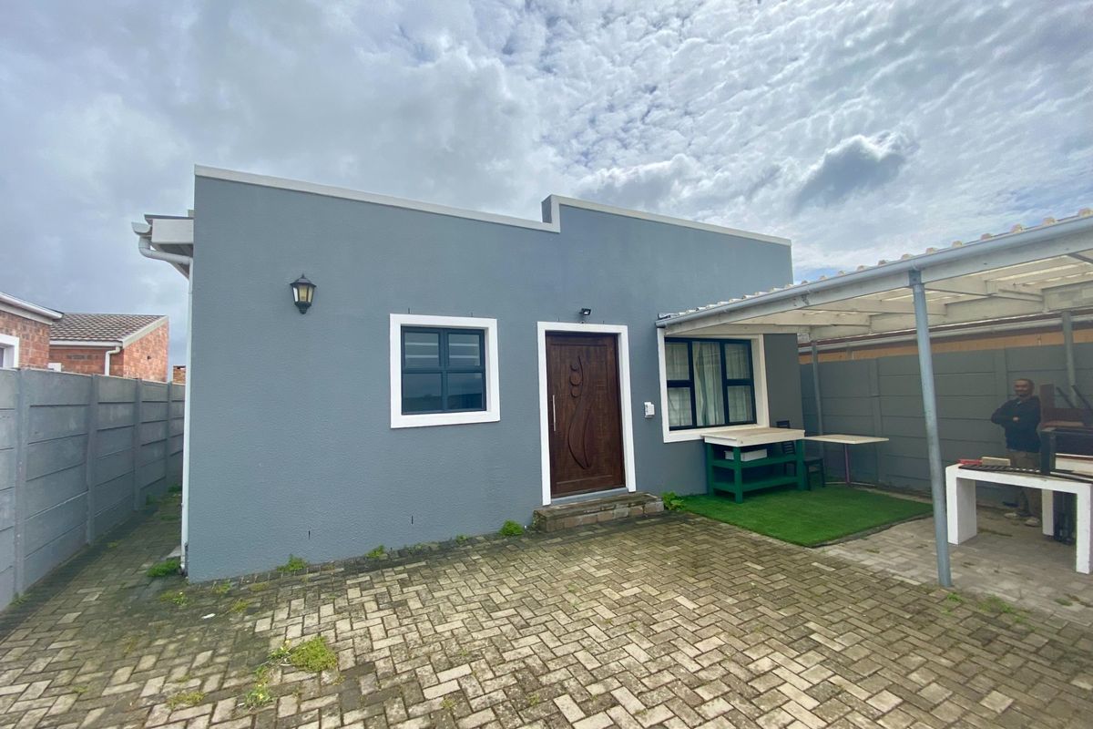 Rear exterior view featuring a paved courtyard, covered patio area with a built-in braai, and secure boundary walling.