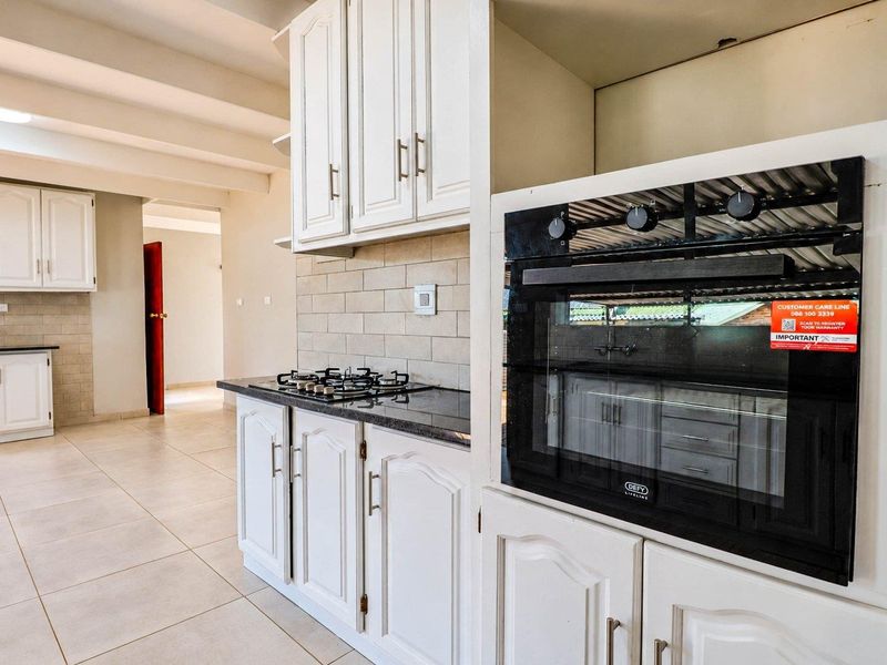 A clean, modern kitchen featuring white cabinetry, granite countertops, a built-in oven, and a gas hob with a neutral tiled backsplash.