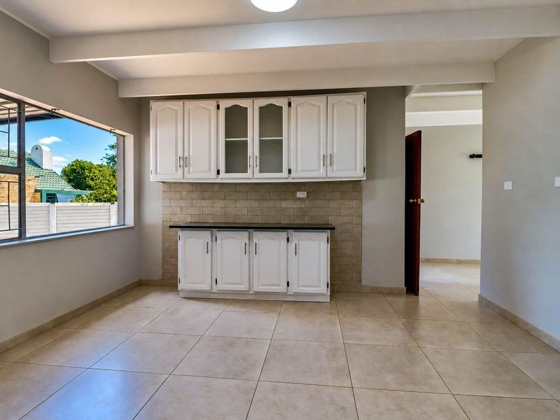 A clean and functional scullery area featuring white built-in cabinetry, a tiled backsplash, and neutral floor tiles, offering ample storage and prep space.