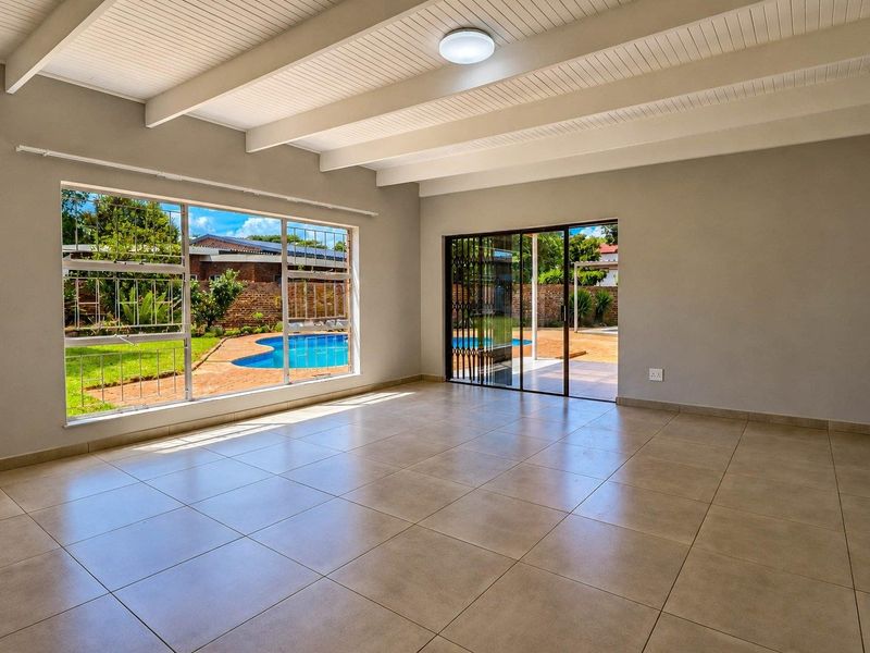Spacious living area featuring exposed beam ceilings, large windows with pool views, and direct access to the outdoor patio area.
