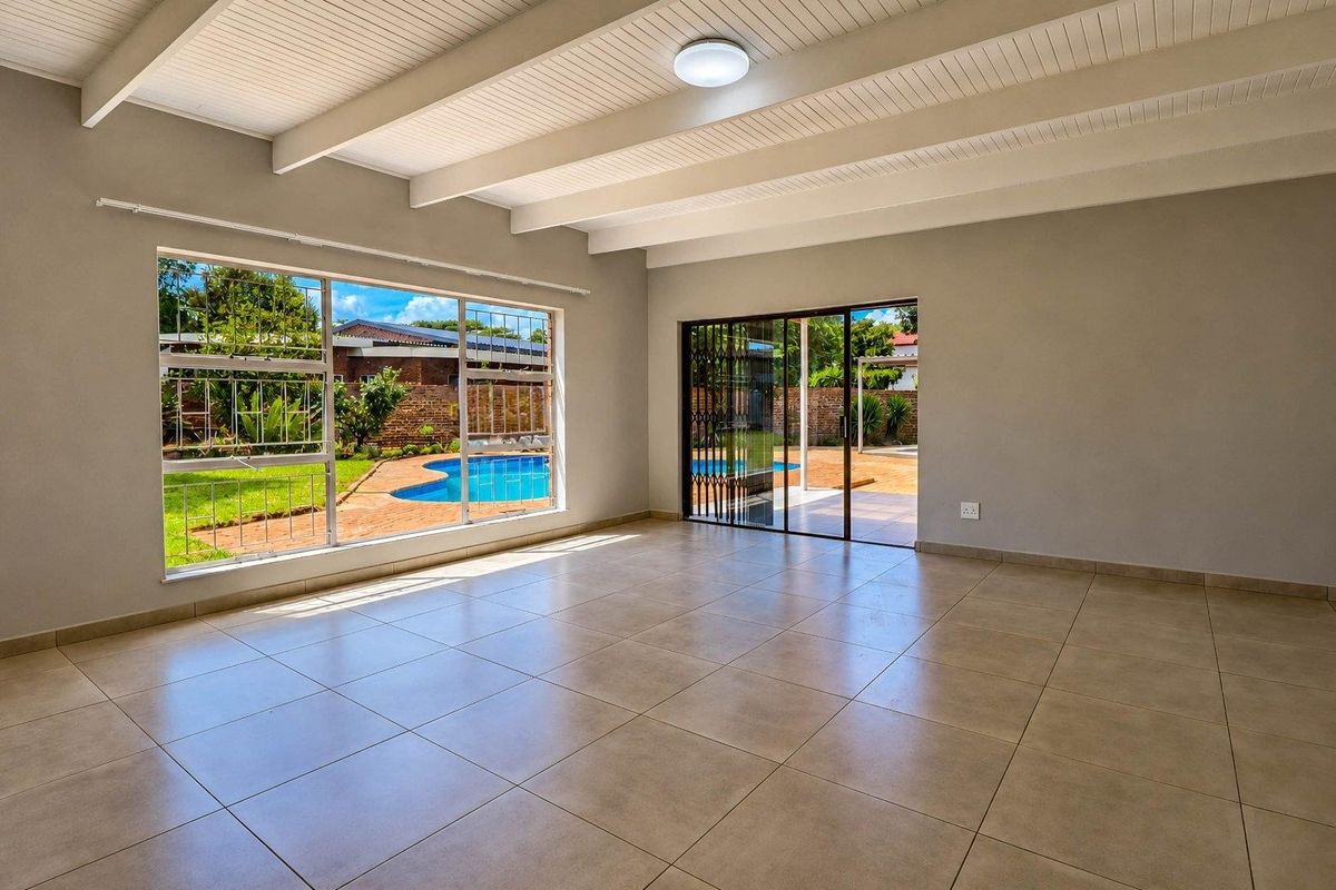 Spacious living area featuring exposed beam ceilings, large windows with pool views, and direct access to the outdoor patio area.