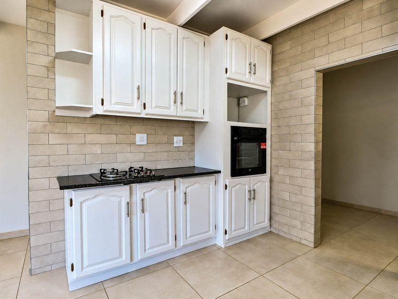 A clean, modern kitchen featuring white cabinetry, granite countertops, a built-in gas hob, and an integrated oven with neutral tiled finishes.