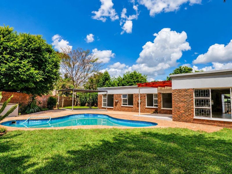 Rear exterior view featuring a swimming pool, paved patio area, pergola, and established garden with brick boundary walls.