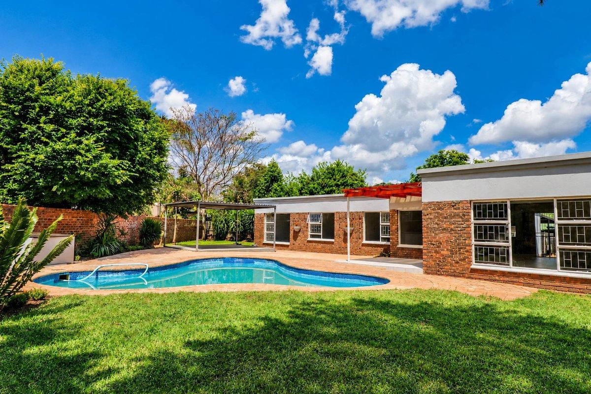 Rear exterior view featuring a swimming pool, paved patio area, pergola, and established garden with brick boundary walls.
