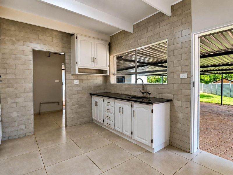 A clean, functional kitchen featuring tiled walls and flooring, white cabinetry, granite countertops, and an integrated oven, with direct access to an outdoor area.