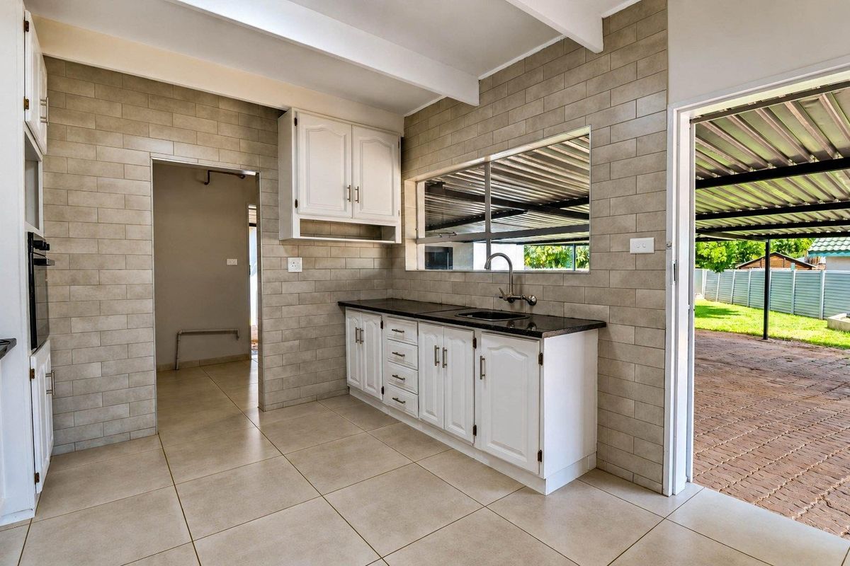 A clean, functional kitchen featuring tiled walls and flooring, white cabinetry, granite countertops, and an integrated oven, with direct access to an outdoor area.