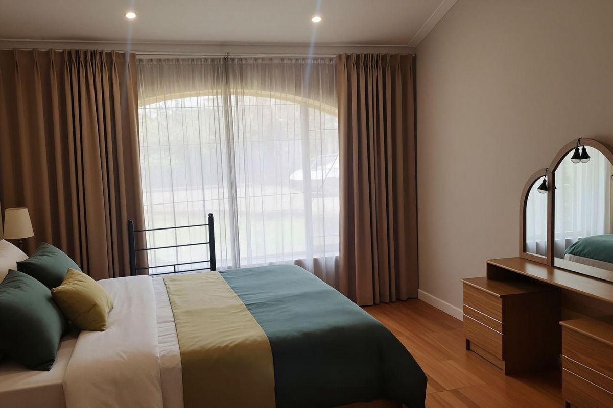 A well-maintained bedroom featuring timber flooring, recessed downlighting, and a large arched window with floor-to-ceiling curtains.