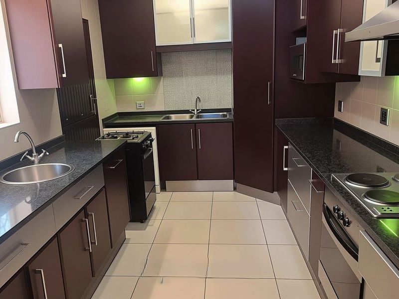 Modern kitchen featuring dark wood cabinetry, granite countertops, integrated appliances, and a mosaic tile backsplash, offering a functional and well-maintained cooking space.
