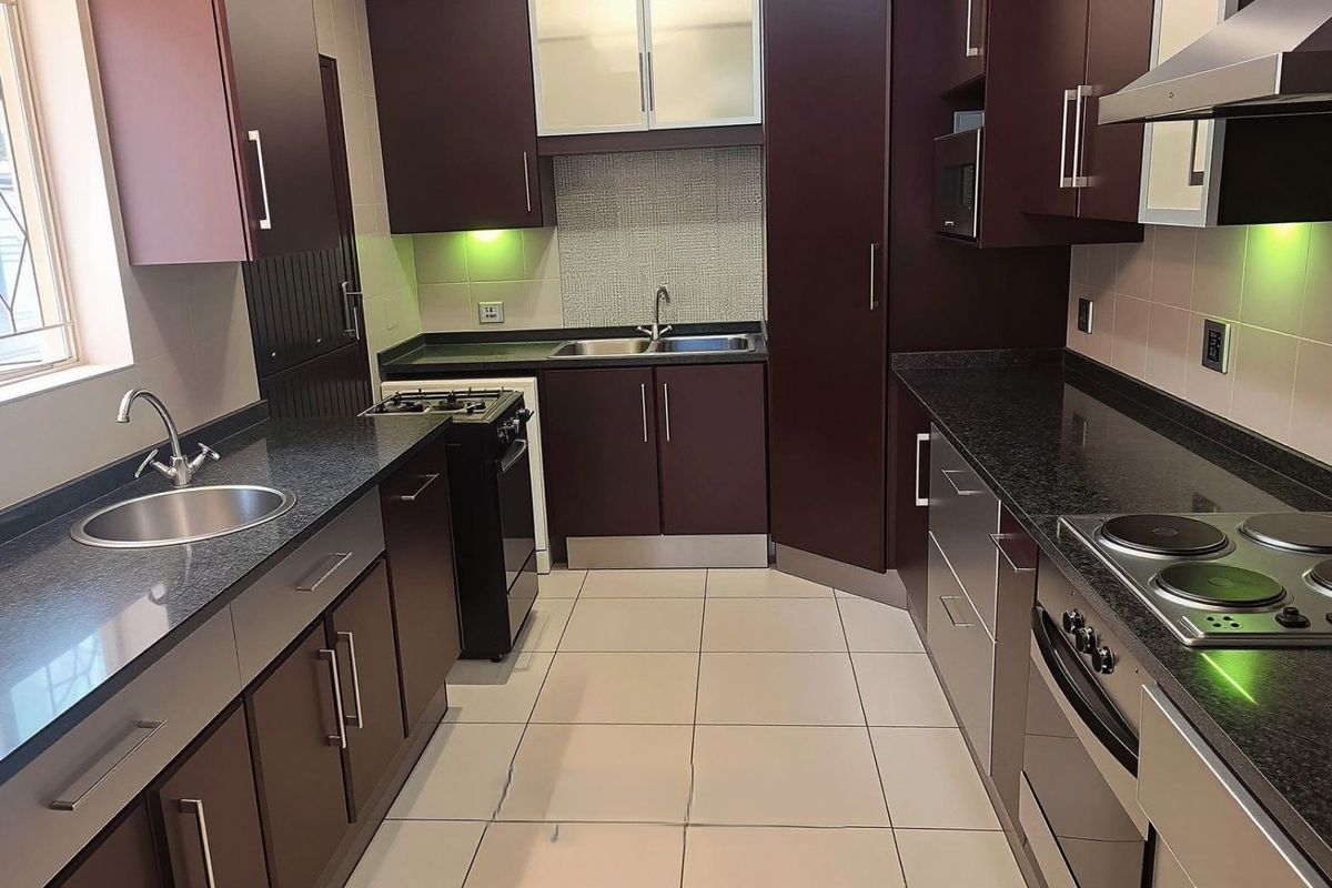 Modern kitchen featuring dark wood cabinetry, granite countertops, integrated appliances, and a mosaic tile backsplash, offering a functional and well-maintained cooking space.