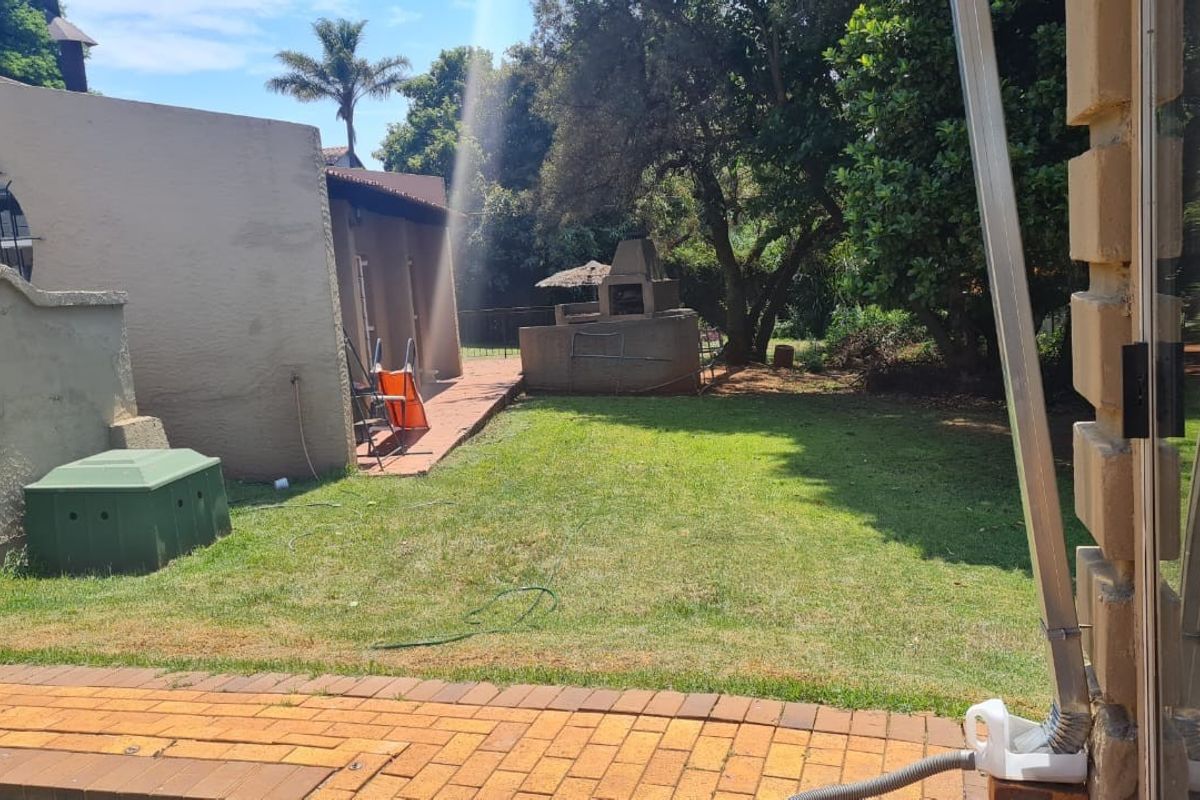 A rear garden area featuring a paved patio, a built-in braai, and a lawn, providing a functional outdoor space for entertainment.