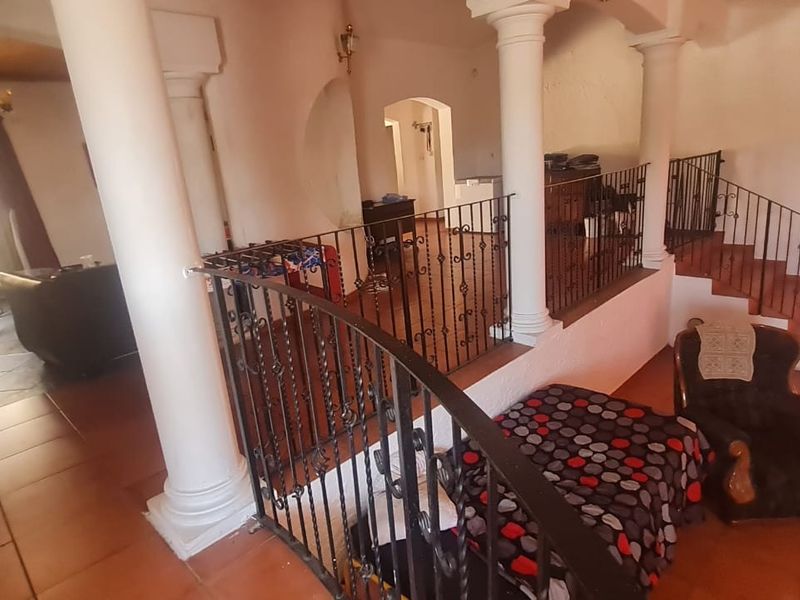 Spacious split-level living area featuring classical columns, wrought iron balustrades, and tiled flooring, offering a unique architectural layout with potential for modernization.