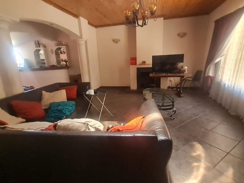 Spacious living room featuring a fireplace, timber ceiling, and tiled flooring, with an open-plan layout connecting to an adjacent area via an arched opening.