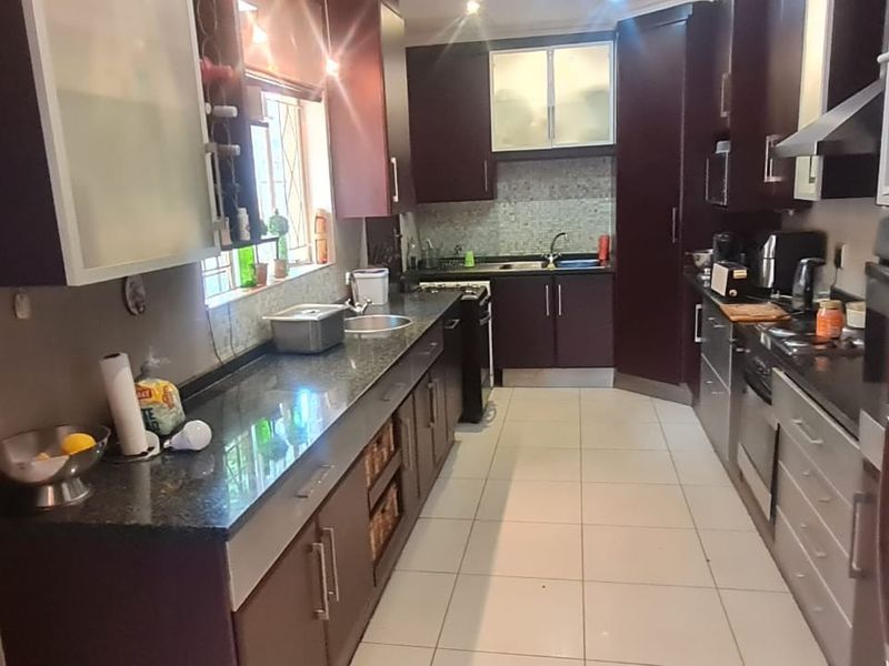 A functional galley-style kitchen featuring dark wood cabinetry, granite countertops, a mosaic tile backsplash, and tiled flooring with integrated appliances.