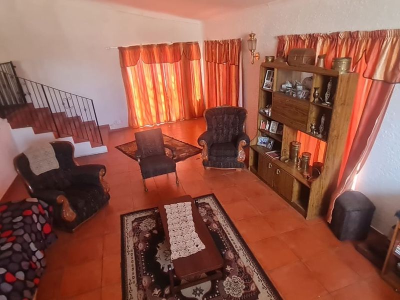 Spacious living area featuring terracotta floor tiles, textured walls, and a wrought iron staircase railing leading to the upper level.