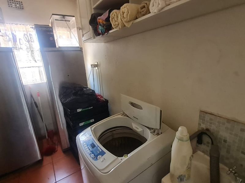 A functional laundry area featuring a utility sink, tiled splashback, and built-in shelving, providing practical space for washing and storage needs.
