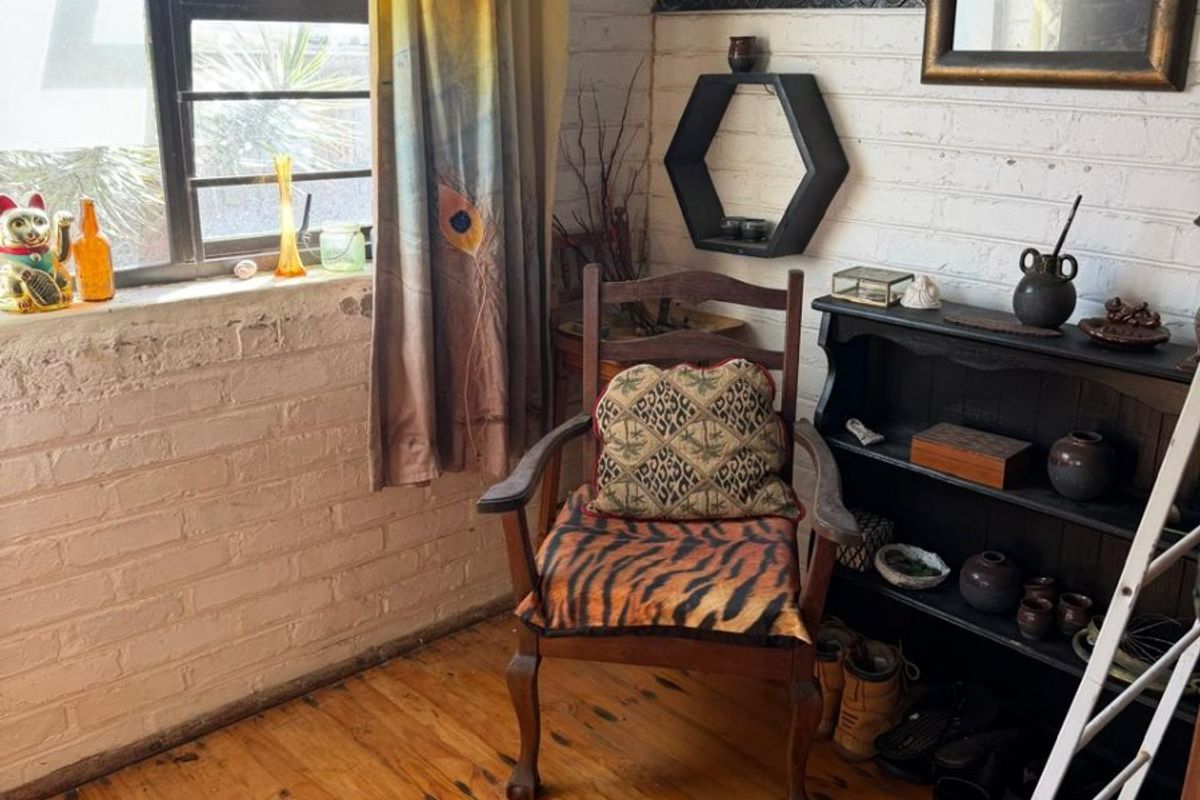 A cozy living space featuring exposed painted brick walls, original timber flooring, and a large steel-framed window providing natural light.