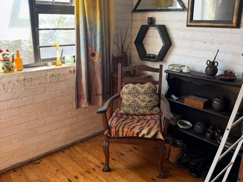 A cozy living space featuring exposed painted brick walls, original timber flooring, and a large steel-framed window providing natural light.