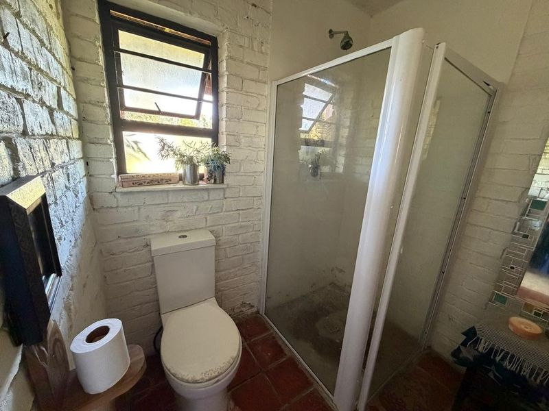 A compact bathroom featuring exposed white brick walls, a tiled floor, a corner shower enclosure, and a standard toilet.