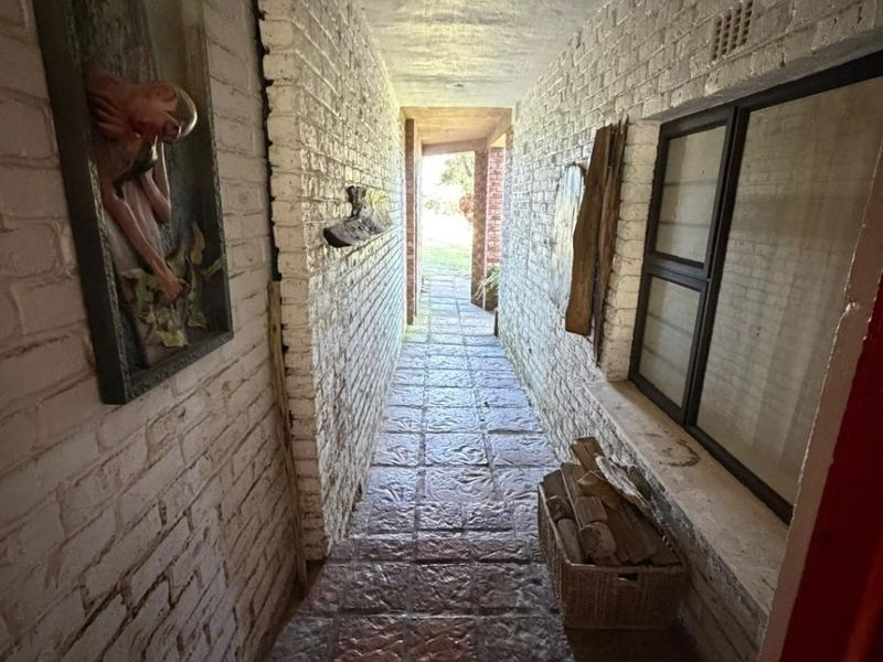 A narrow hallway featuring exposed white-painted brick walls, tiled flooring, and recessed lighting, leading towards an outdoor area.