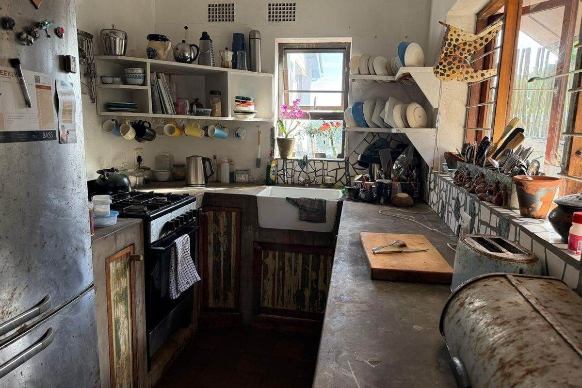 A rustic kitchen featuring concrete countertops, a farmhouse sink, gas stove, and open shelving, offering a character-filled space with potential for modernization.