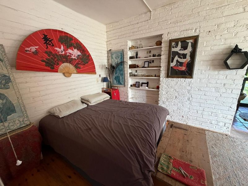 Bedroom featuring exposed white-painted brick walls, built-in wall shelving, and timber flooring, offering a rustic aesthetic.