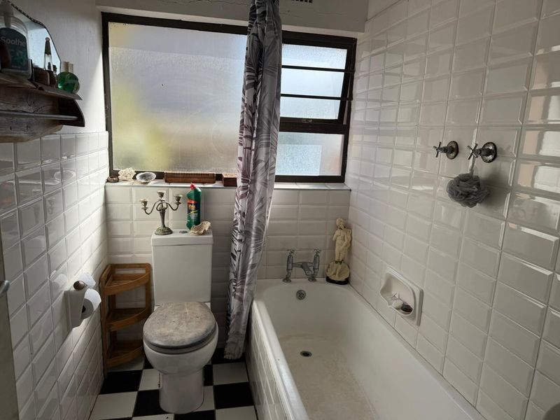 A compact bathroom featuring a bathtub, toilet, and classic white wall tiling with a checkered floor, offering potential for a modern renovation.