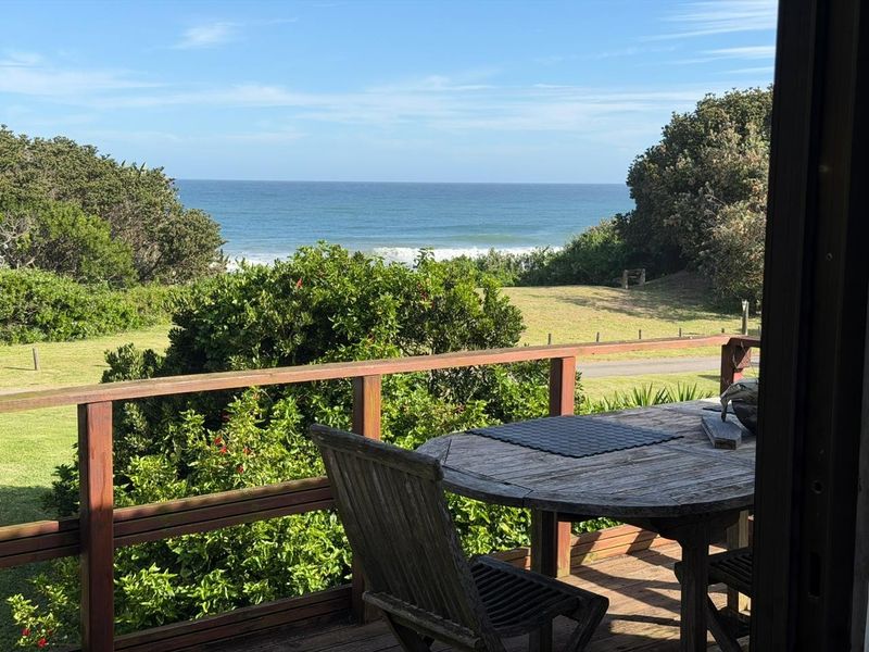 A wooden balcony deck featuring a timber balustrade, offering scenic views of the surrounding greenery and the ocean.