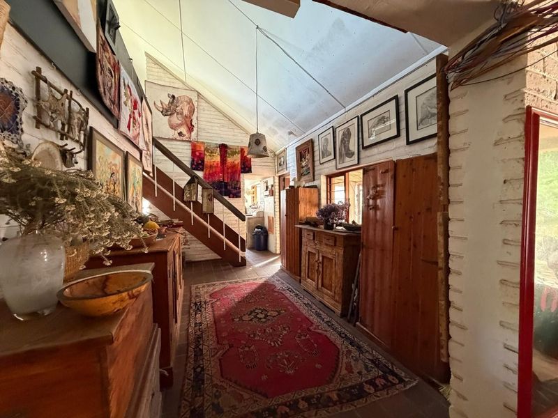 A rustic hallway featuring exposed brick walls, a vaulted ceiling, and a timber staircase, providing a unique character-filled entrance to the home.