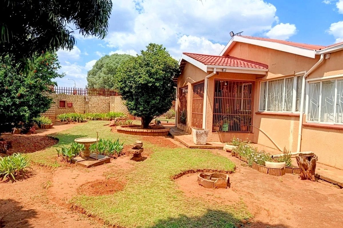 A view of the rear garden featuring a tiled roof house, security bars on windows, and a landscaped yard with a brick boundary wall.