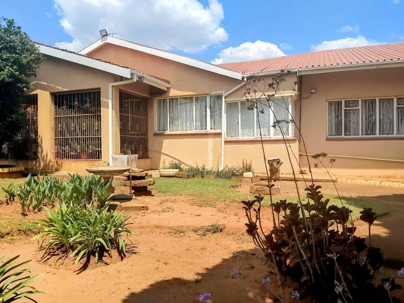 Rear view of the house featuring plastered walls, a corrugated metal roof, and security-barred windows overlooking a garden area.