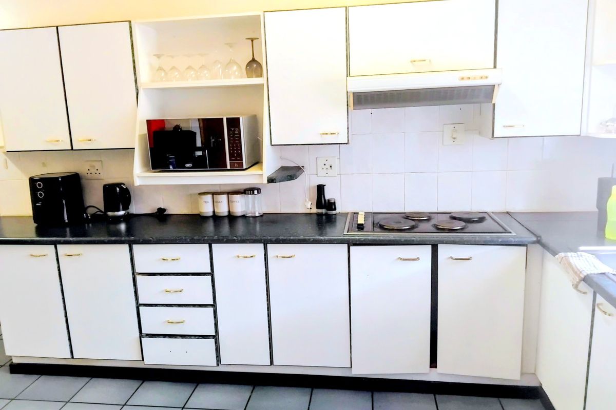 A functional kitchen featuring white cabinetry, dark laminate countertops, an integrated electric hob with extractor fan, and tiled flooring.