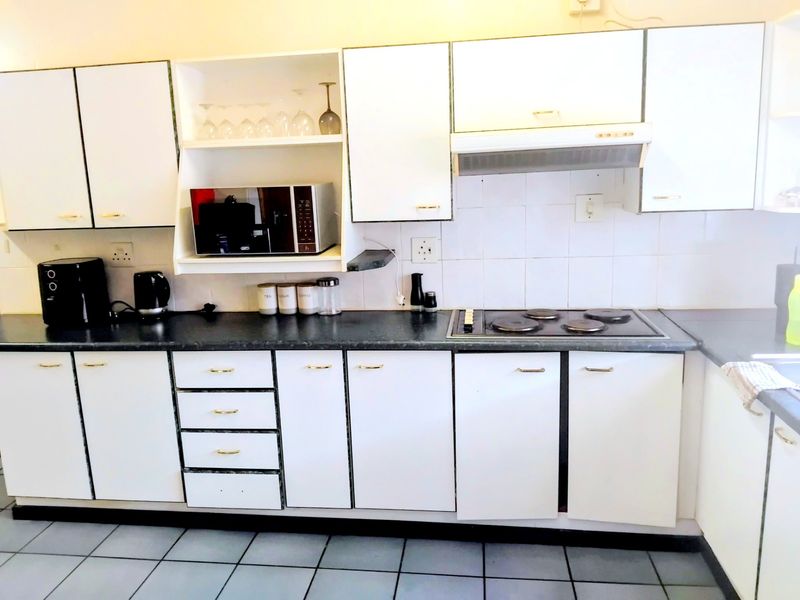 A functional kitchen featuring white cabinetry, dark laminate countertops, an integrated electric hob with extractor fan, and tiled flooring.