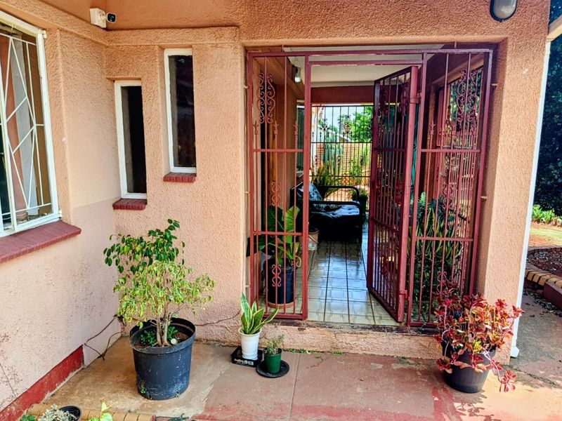A covered patio area featuring tiled flooring and a security gate, providing a functional outdoor transition space with potential for cosmetic updates.