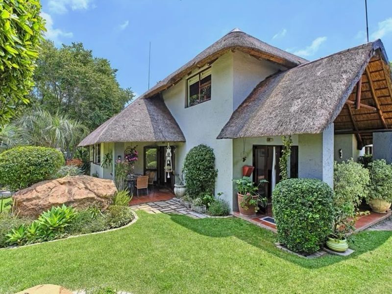 Rear view of a townhouse featuring a traditional thatched roof, a covered patio area, and a well-maintained landscaped garden with a large feature rock.