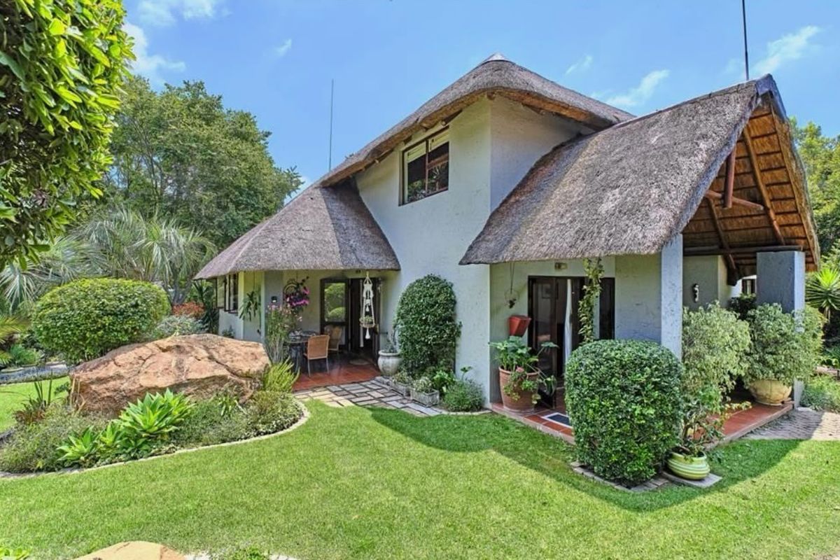 Rear view of a townhouse featuring a traditional thatched roof, a covered patio area, and a well-maintained landscaped garden with a large feature rock.
