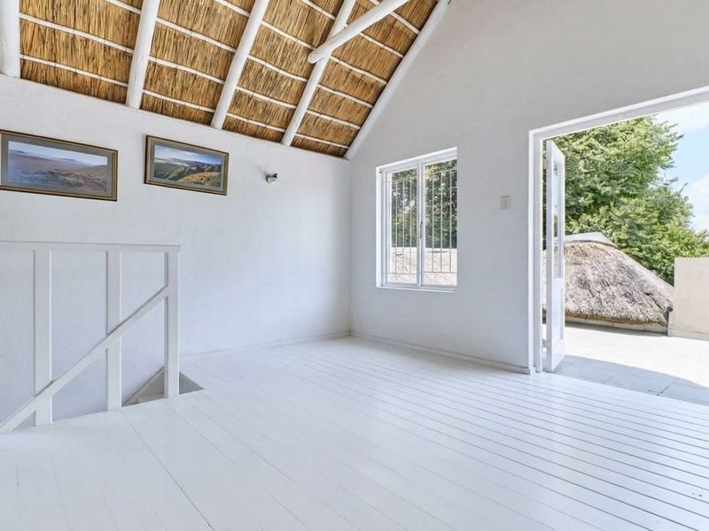 Bright and airy bedroom featuring an exposed thatch ceiling with timber rafters, painted timber flooring, and direct access to a private balcony.