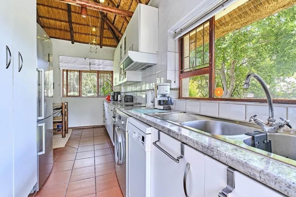 A functional kitchen featuring granite countertops, stainless steel sink, and exposed timber beams under a traditional thatch roof, offering a rustic aesthetic.