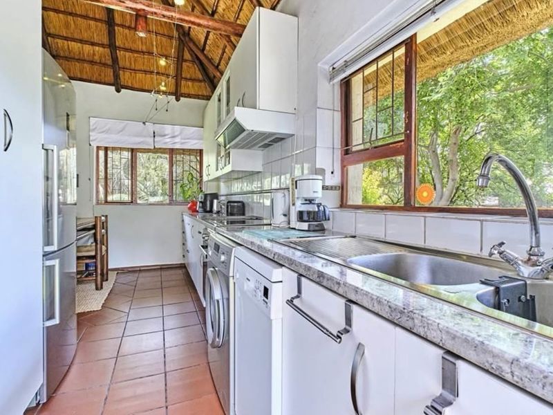 A functional kitchen featuring granite countertops, stainless steel sink, and exposed timber beams under a traditional thatch roof, offering a rustic aesthetic.