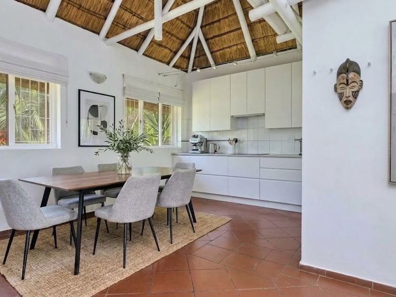 Open-plan kitchen and dining area featuring a unique thatched roof with exposed rafters, modern white cabinetry, and terracotta tiled flooring.